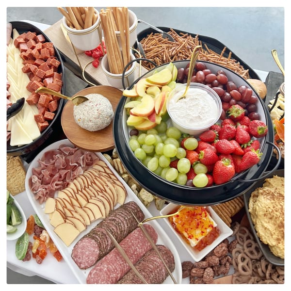 A large deli platter with cheeses, meats, fruits, dips, and various snacks.