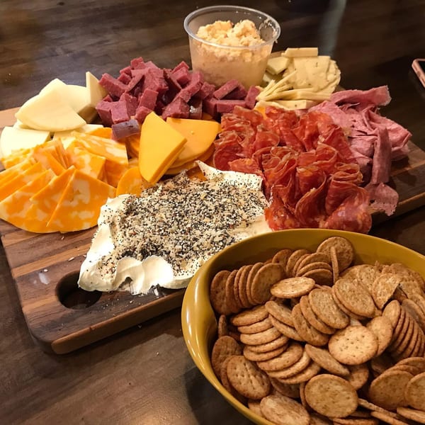 A deli charcuterie board with various cheeses, meats, and a bowl of crackers.