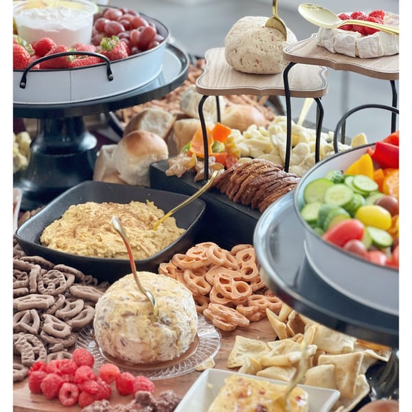 A deli spread with various cheeses, fruits, vegetables, breads, and dips on a tiered serving platter.