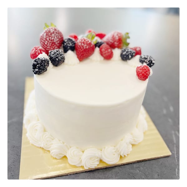 White frosted cake topped with fresh strawberries, raspberries, and blackberries, dusted with powdered sugar.