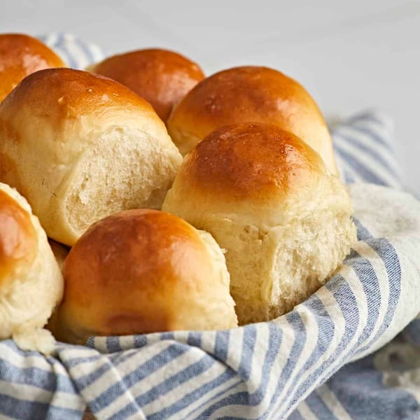 Golden brown dinner rolls in a basket lined with a blue and white striped cloth.