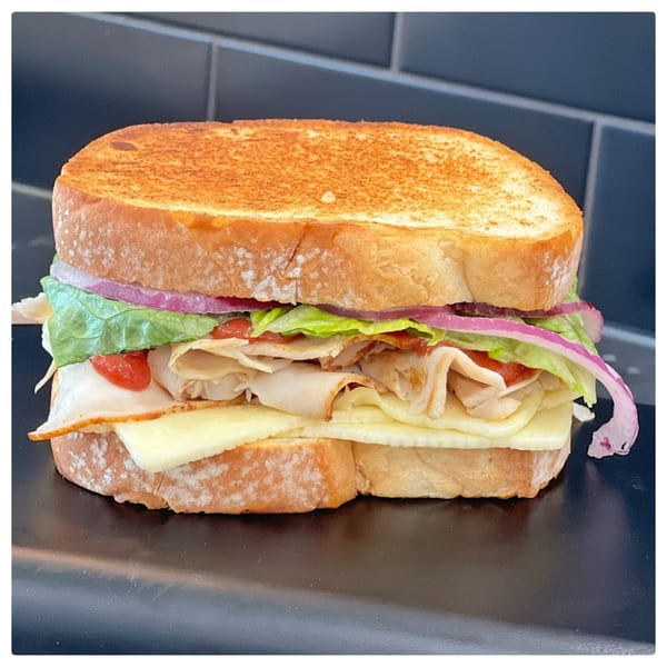 A deli sandwich with turkey, cheese, lettuce, red onion, and tomato on toasted bread.