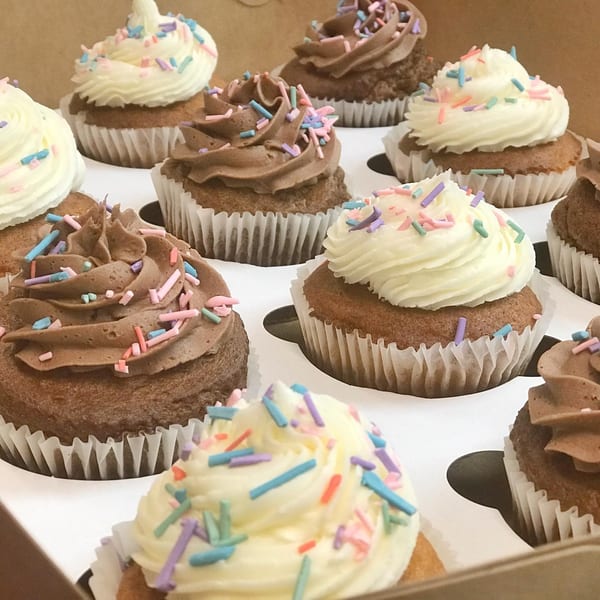 A box of cupcakes with white and chocolate frosting, topped with colorful sprinkles.